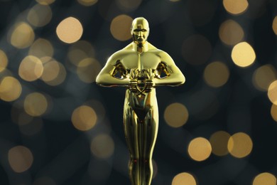 Photo of Golden trophy in shape of human figure on dark background with blurred lights