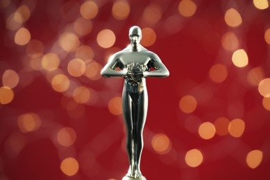 Photo of Golden trophy in shape of human figure on red background with blurred lights