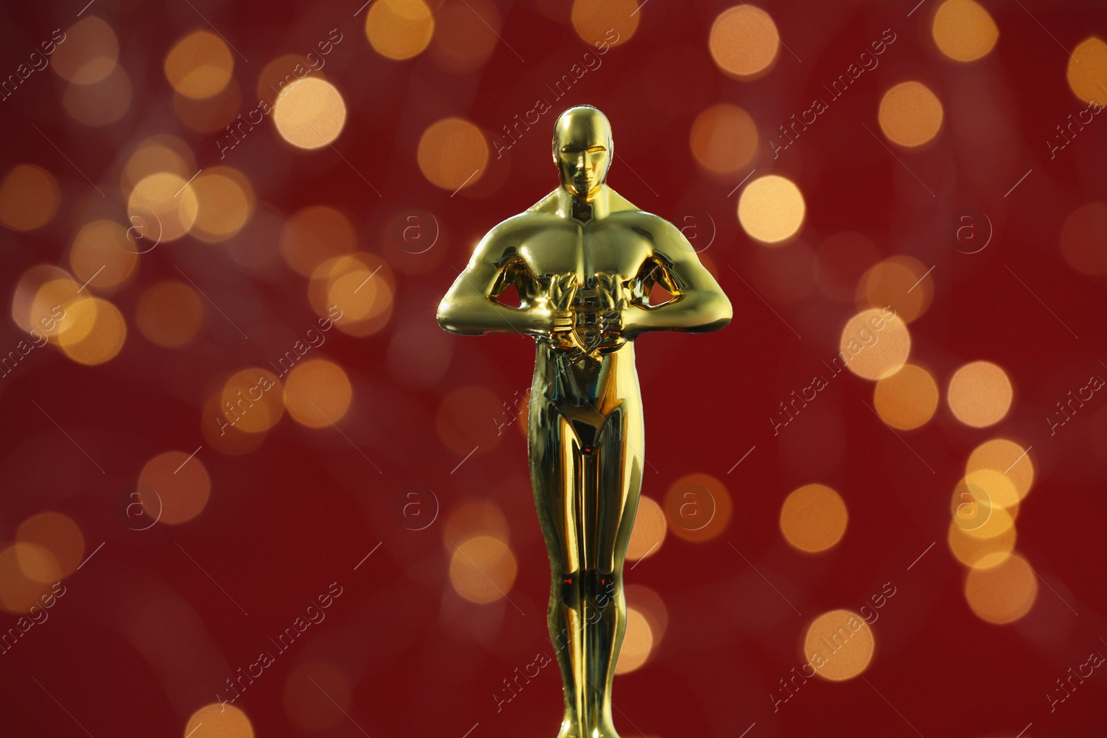 Photo of Golden trophy in shape of human figure on red background with blurred lights