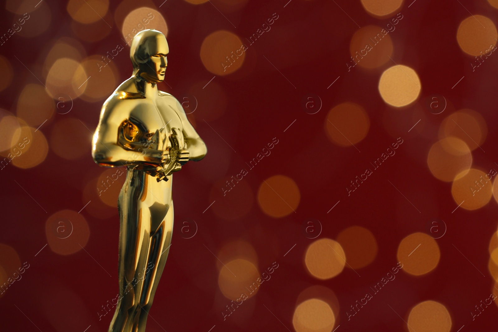 Photo of Golden trophy in shape of human figure on red background with blurred lights, space for text