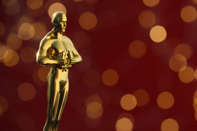 Photo of Golden trophy in shape of human figure on red background with blurred lights, space for text