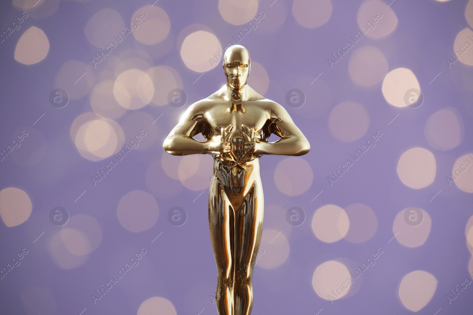 Photo of Golden trophy in shape of human figure on purple background with blurred lights