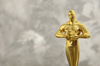 Photo of Golden trophy in shape of human figure against blurred gray background, space for text