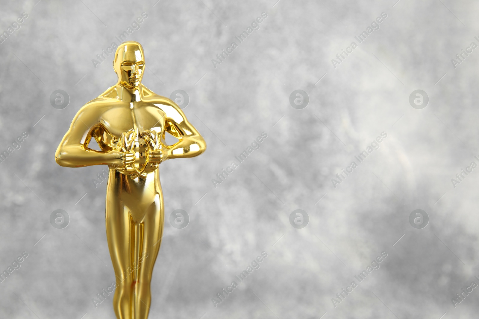 Photo of Golden trophy in shape of human figure against blurred gray background, space for text