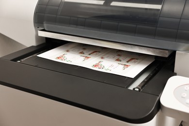 Photo of Modern printer with printed wedding invitation cards indoors, closeup. Printing house