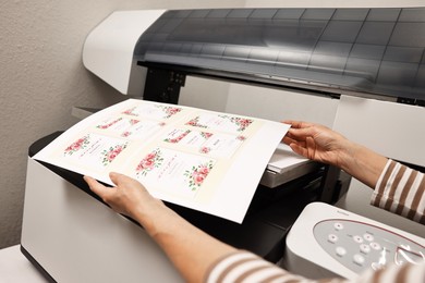 Photo of Woman with printed invitation cards near modern printer indoors, closeup. Printing house