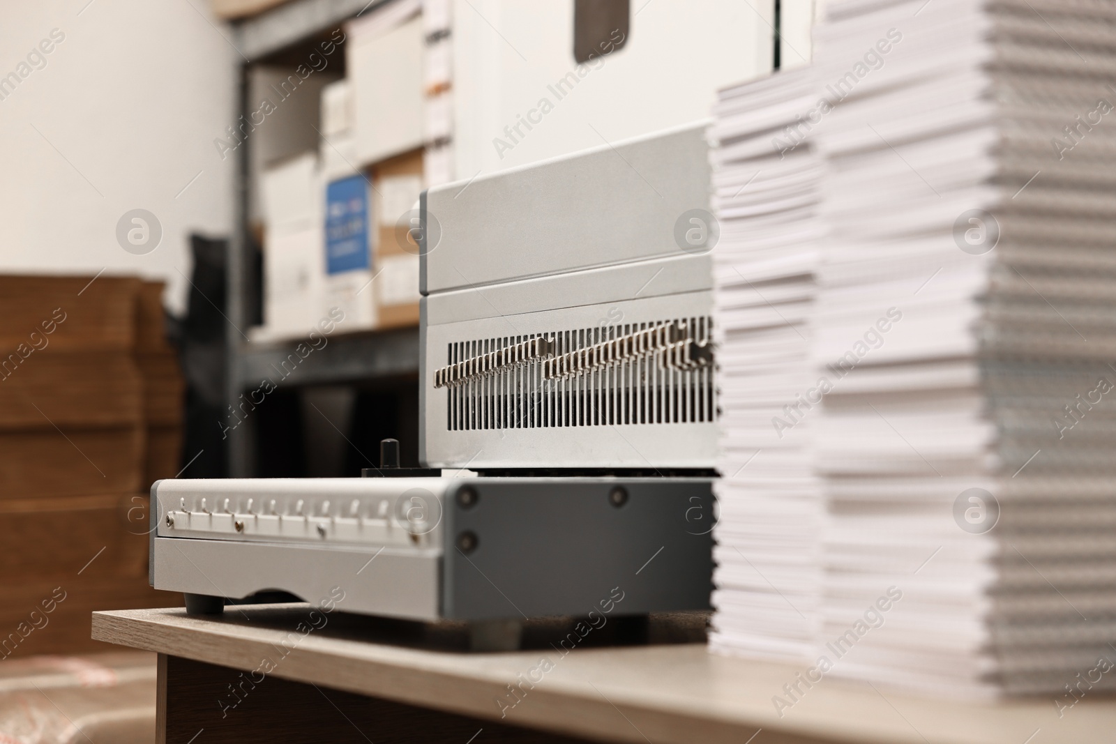 Photo of Modern binding machine and stacks of notebooks on wooden table indoors, selective focus