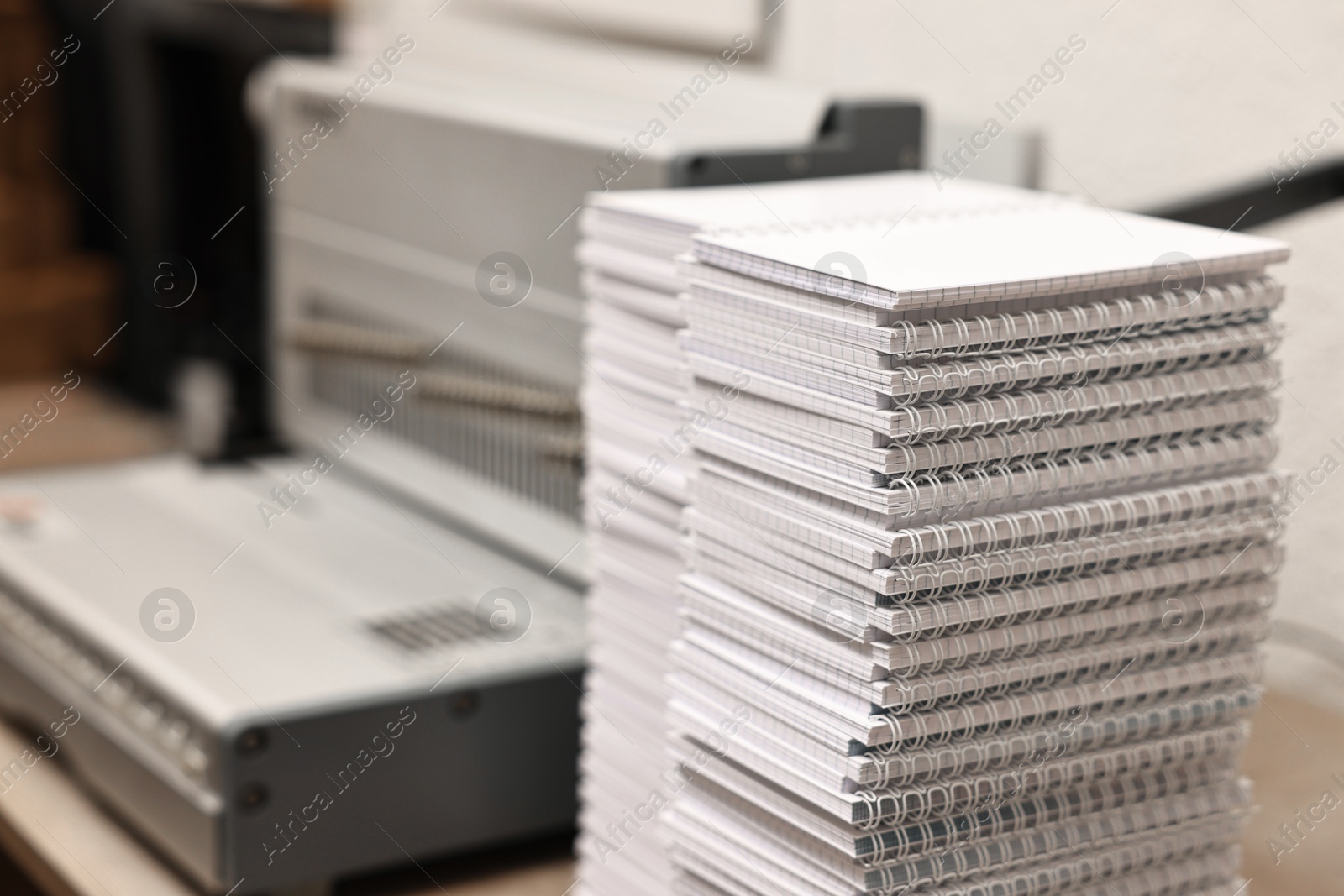 Photo of Modern binding machine and stacks of notebooks on table indoors, selective focus