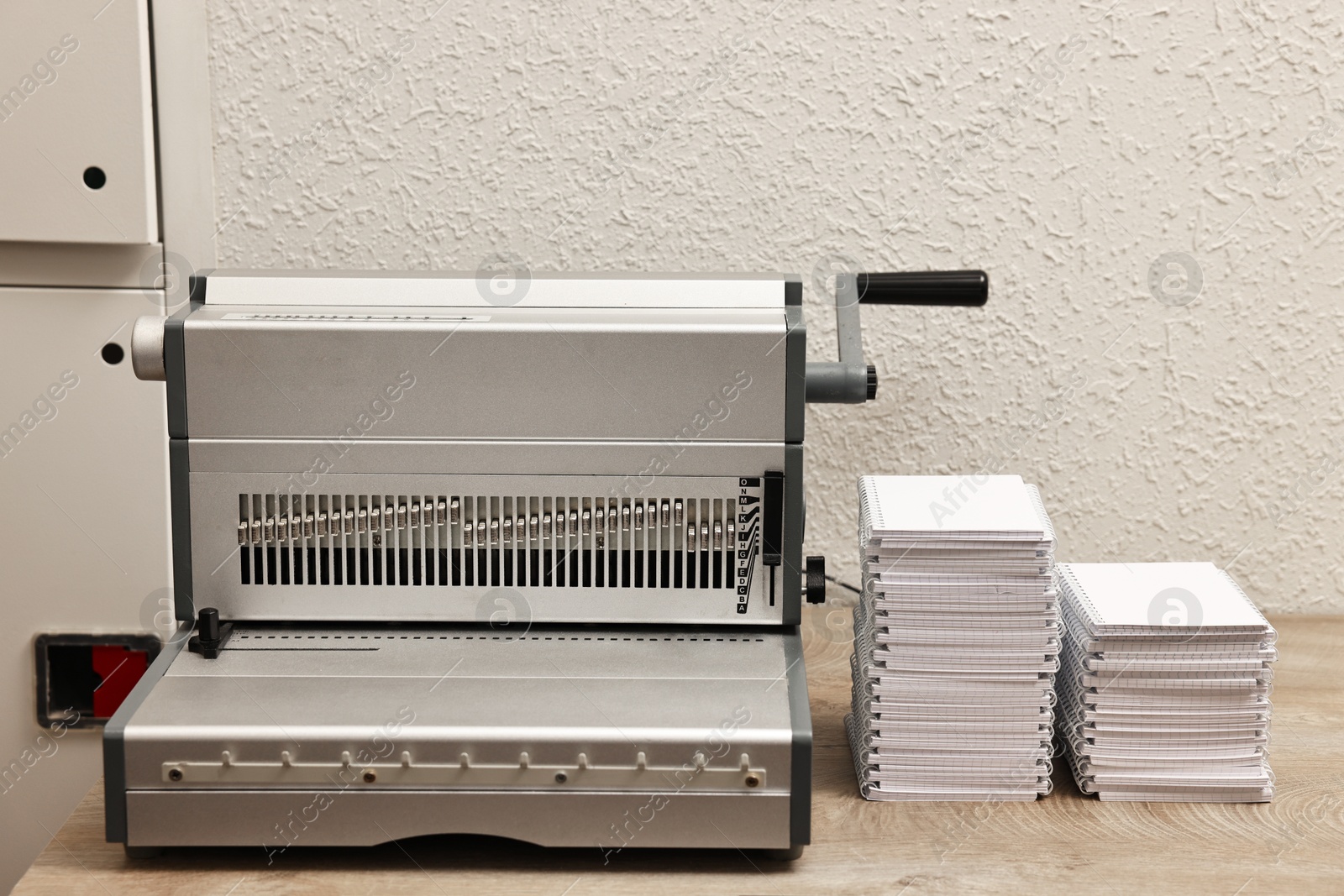 Photo of Modern binding machine and stacks of notebooks on wooden table indoors