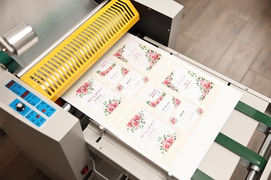 Photo of Modern roll laminator and paper sheet with invitation cards indoors, closeup. Printing house