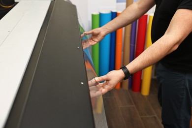 Photo of Man using wide-format printer indoors, closeup. Printing house