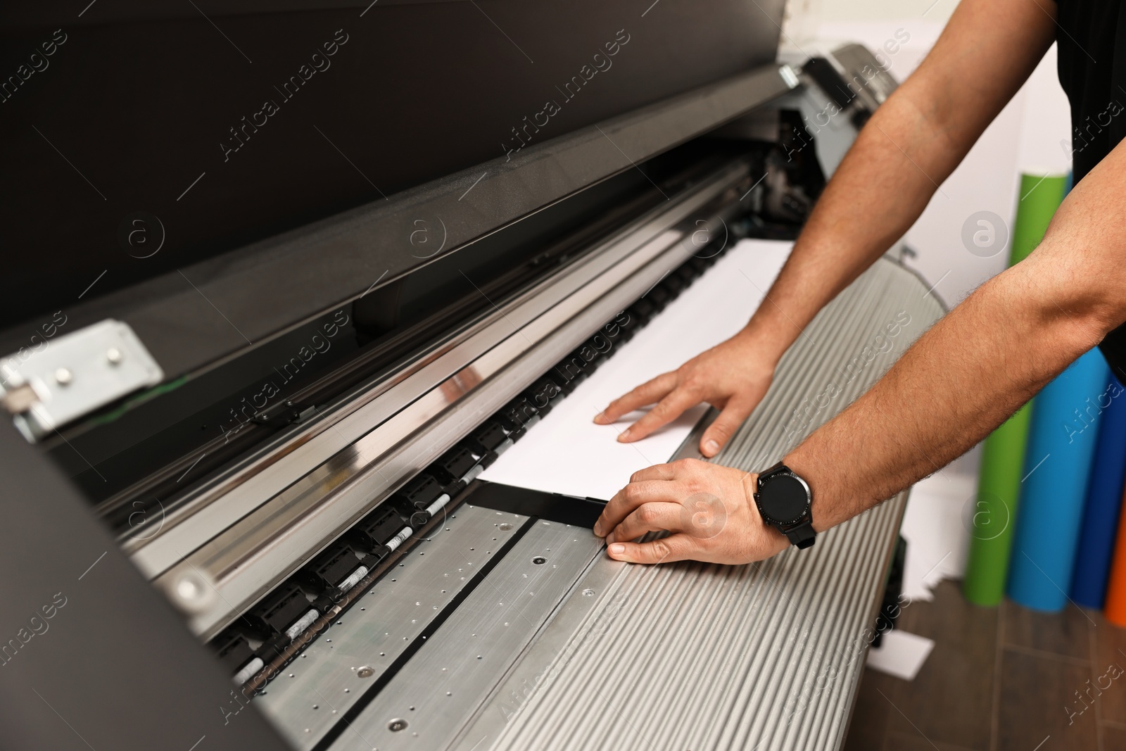 Photo of Man using wide-format printer indoors, closeup. Printing house