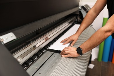 Photo of Man using wide-format printer indoors, closeup. Printing house