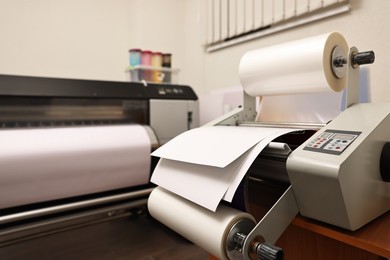 Photo of Modern roll laminator with paper on desk indoors. Printing house