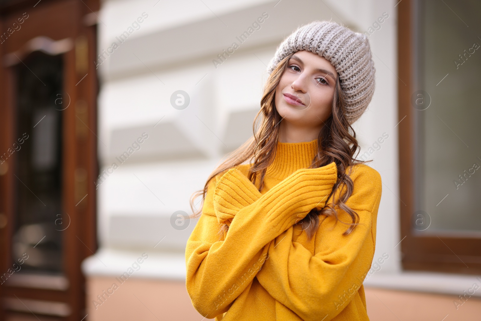 Photo of Beautiful young woman in warm sweater and hat outdoors, space for text. Autumn mood