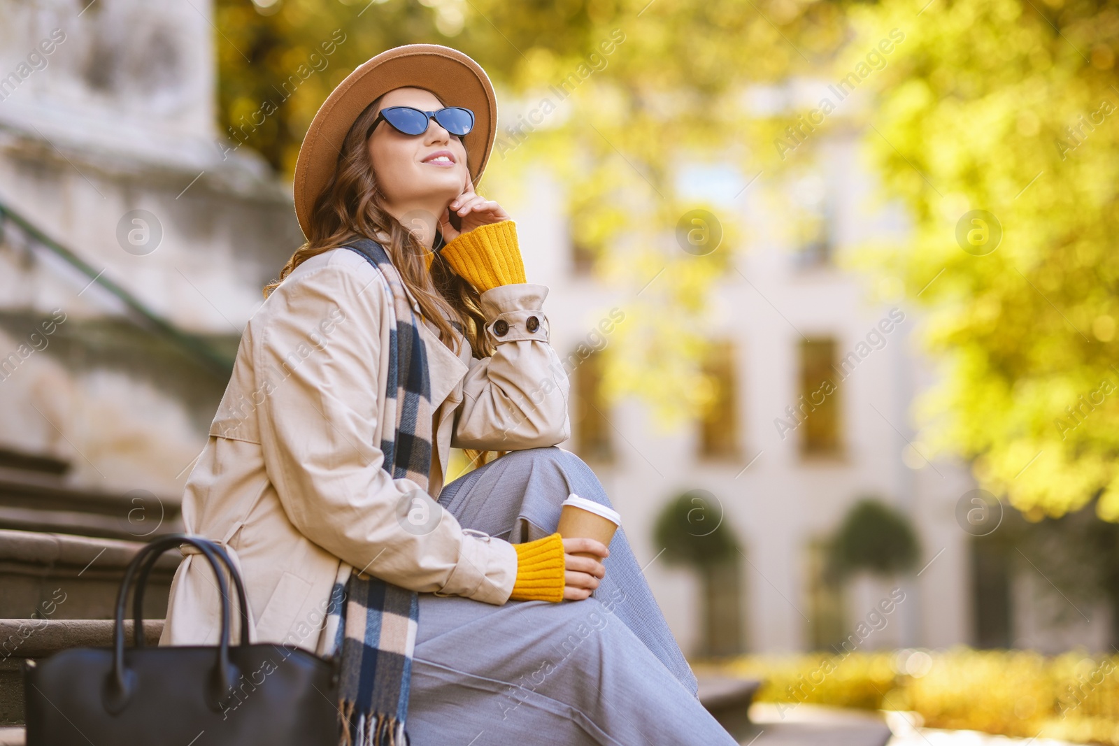 Photo of Charming young woman with cup of coffee on city street, space for text. Autumn season