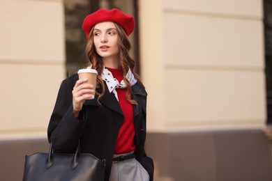 Stylish woman with cup of hot drink outdoors, space for text