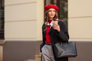 Stylish woman with cup of hot drink outdoors, space for text