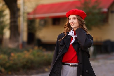 Photo of Stylish young woman with red beret on city street, space for text