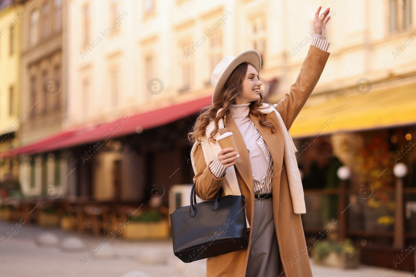 Photo of Beautiful young woman with hot drink on city street, space for text. Autumn style