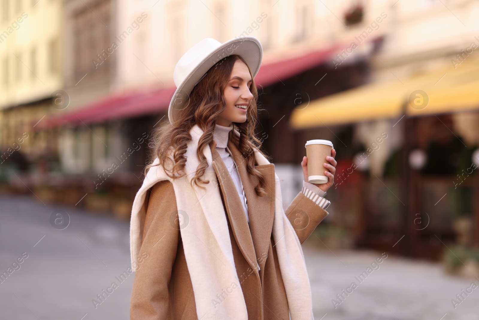 Photo of Beautiful young woman with hot drink on city street. Autumn style