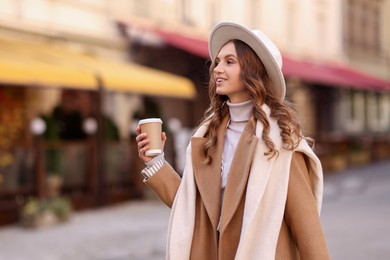 Beautiful young woman with hot drink on city street. Autumn style