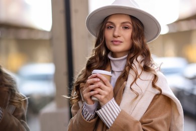 Photo of Charming young woman with hot drink near shop on city street, space for text