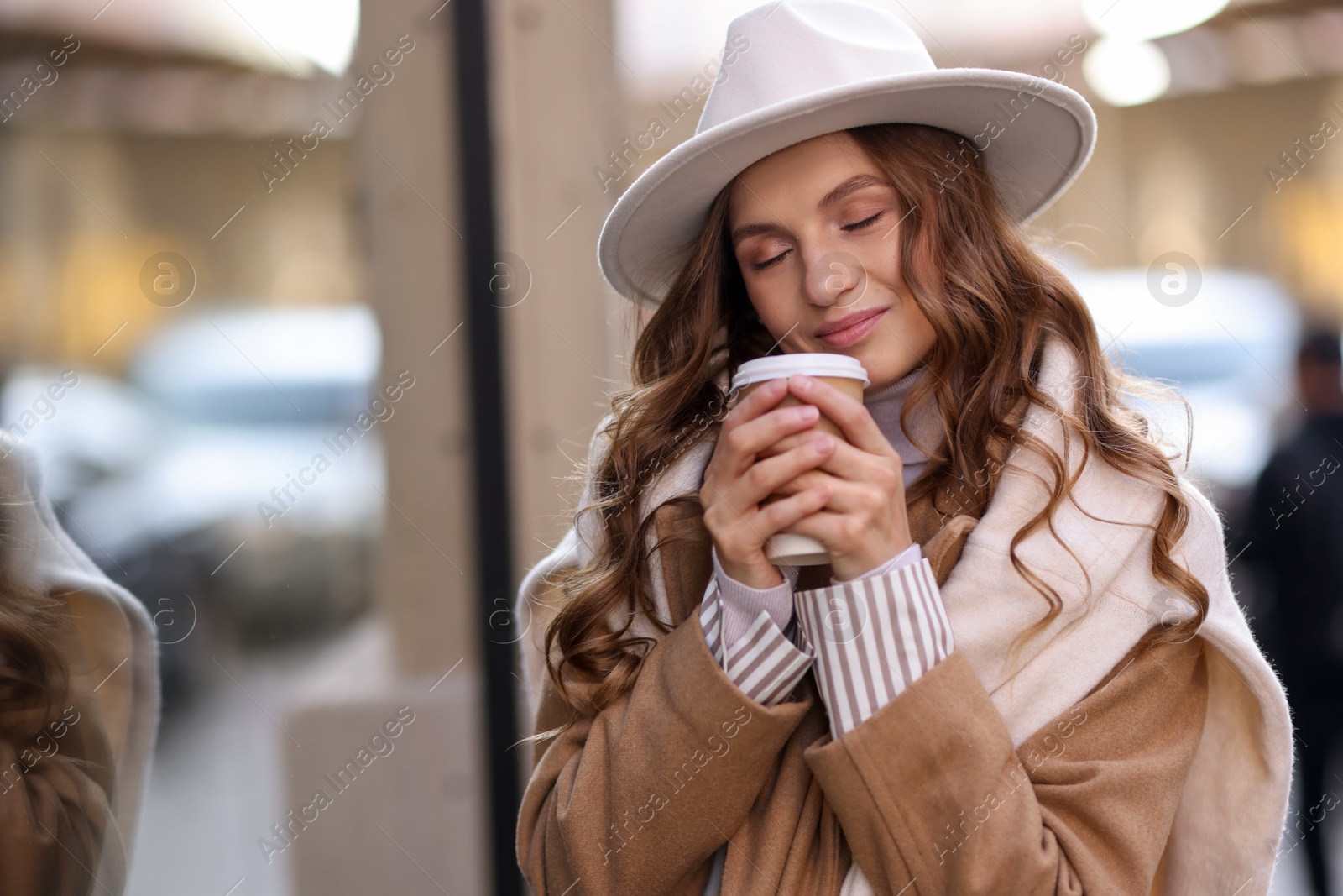 Photo of Charming young woman with hot drink near shop on city street, space for text