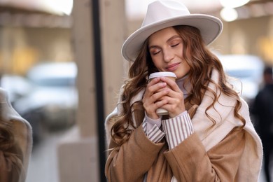 Photo of Charming young woman with hot drink near shop on city street, space for text