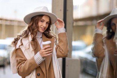 Photo of Charming young woman with hot drink near shop on city street