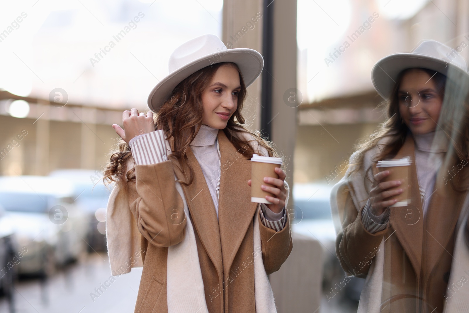 Photo of Charming young woman with hot drink near shop on city street