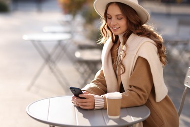 Stylish woman with smartphone in outdoor cafe, space for text. Autumn mood