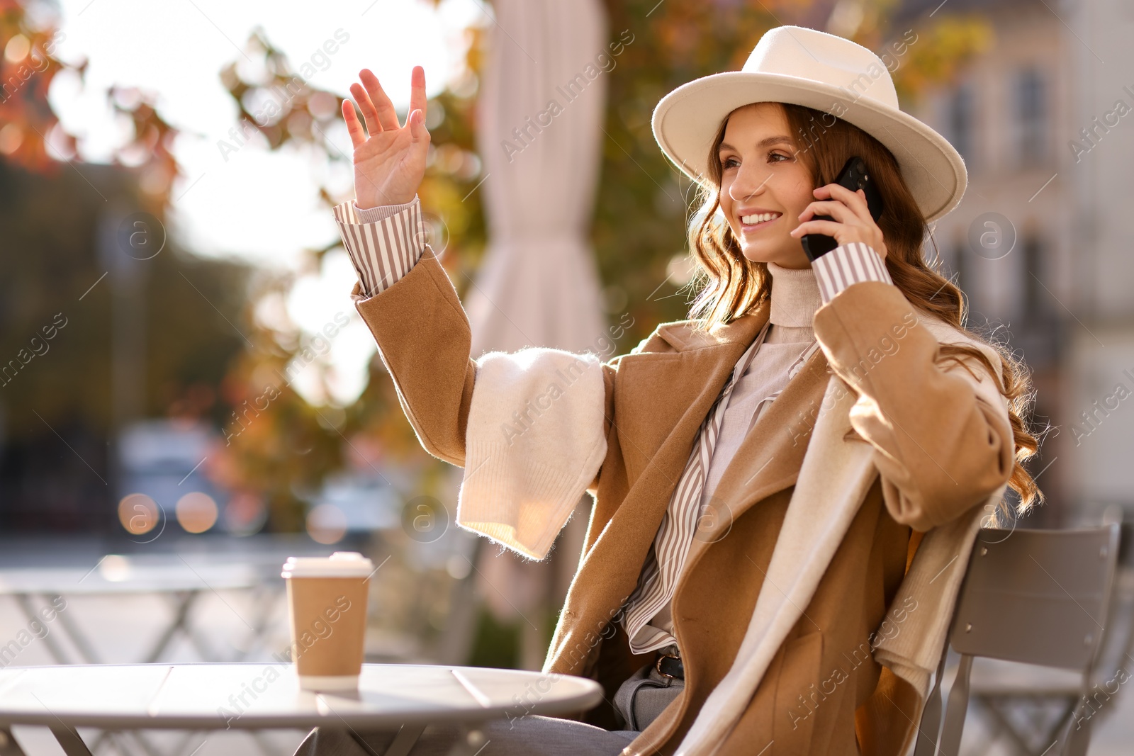 Photo of Stylish woman talking on phone in outdoor cafe. Autumn mood