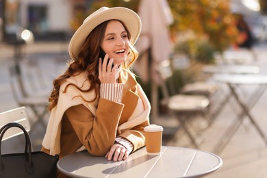 Photo of Stylish woman talking on phone in outdoor cafe. Autumn mood