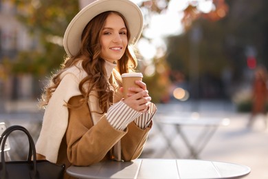 Photo of Stylish woman at table in outdoor cafe, space for text. Autumn mood