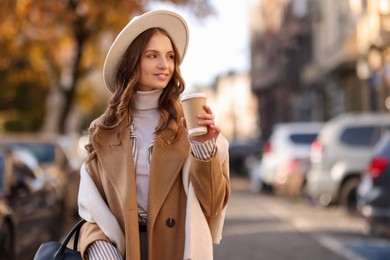 Stylish woman with cup of coffee outdoors, space for text. Autumn mood