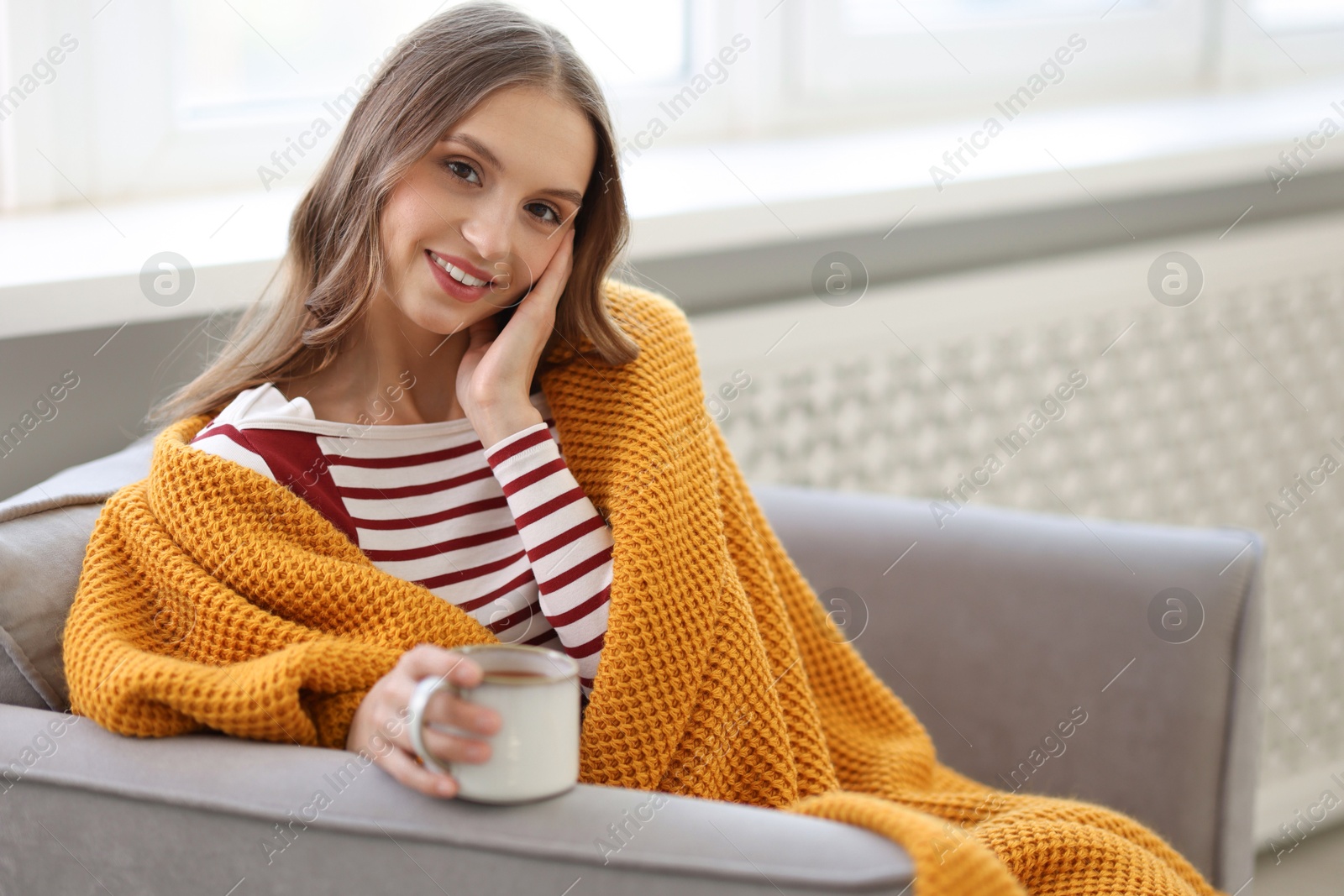 Photo of Charming young woman with cup of hot drink on sofa at home, space for text. Autumn atmosphere