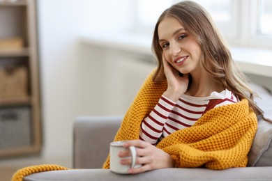 Photo of Charming young woman with cup of hot drink on sofa at home, space for text. Autumn atmosphere