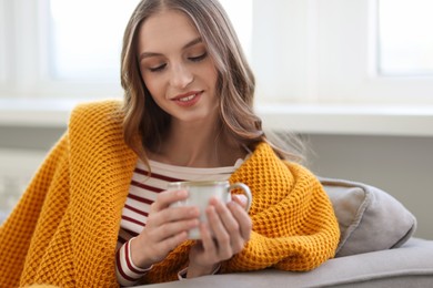 Photo of Charming young woman with cup of hot drink on sofa at home. Autumn atmosphere