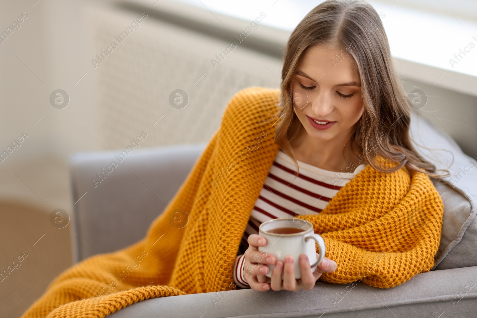 Photo of Charming young woman with cup of hot drink on sofa at home, space for text. Autumn atmosphere