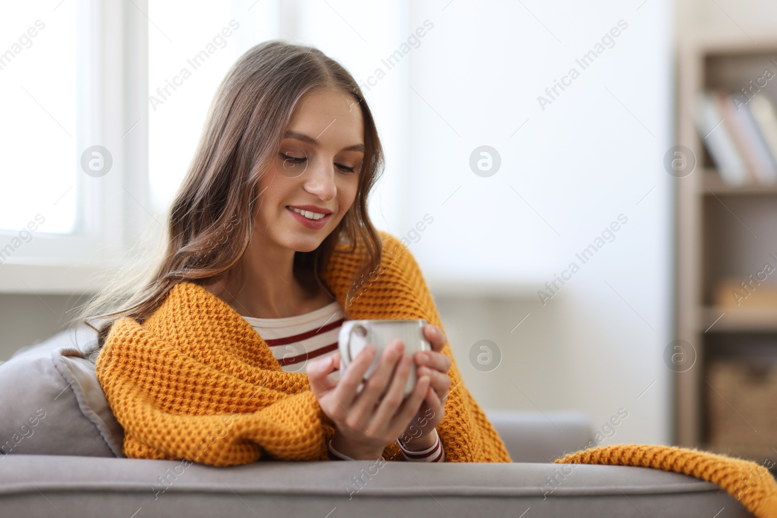 Photo of Charming young woman with cup of hot drink on sofa at home, space for text. Autumn atmosphere