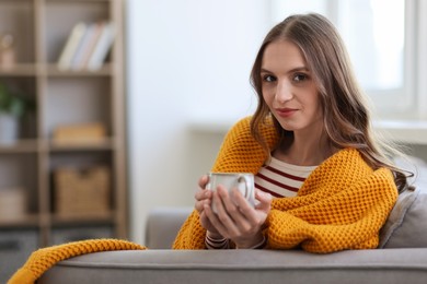 Photo of Charming young woman with cup of hot drink on sofa at home, space for text. Autumn atmosphere