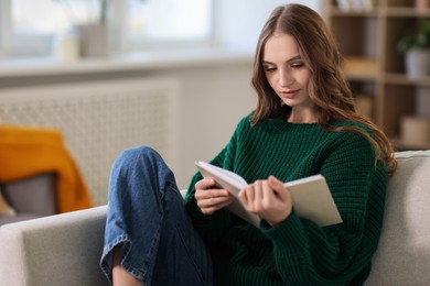 Photo of Charming young woman reading book on sofa at home. Autumn atmosphere