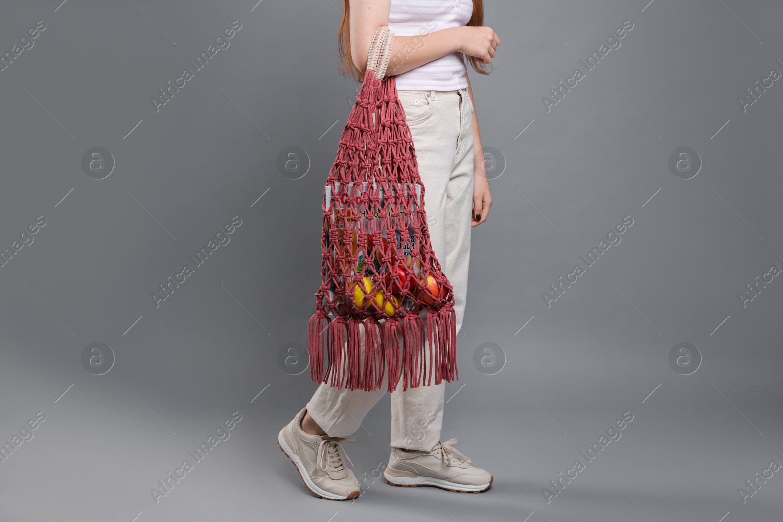 Photo of Teenage girl with handmade macrame bag on grey background, closeup