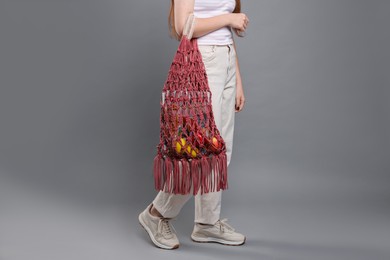 Teenage girl with handmade macrame bag on grey background, closeup