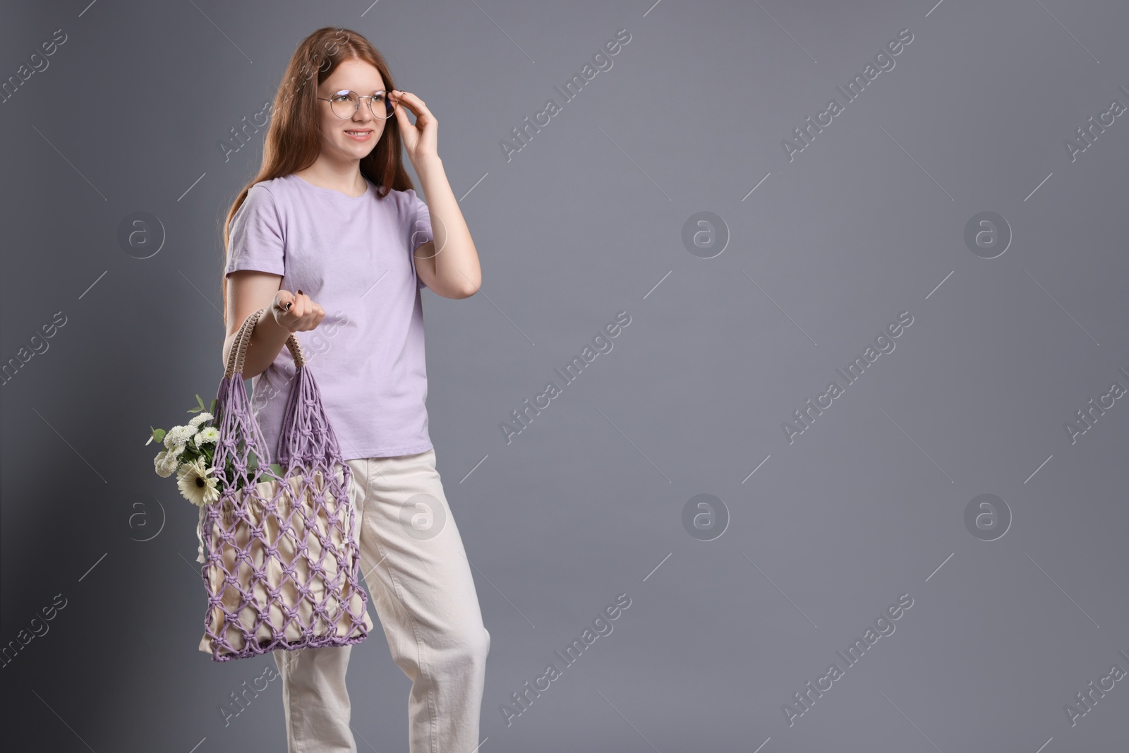 Photo of Teenage girl with handmade macrame bag on grey background. Space for text