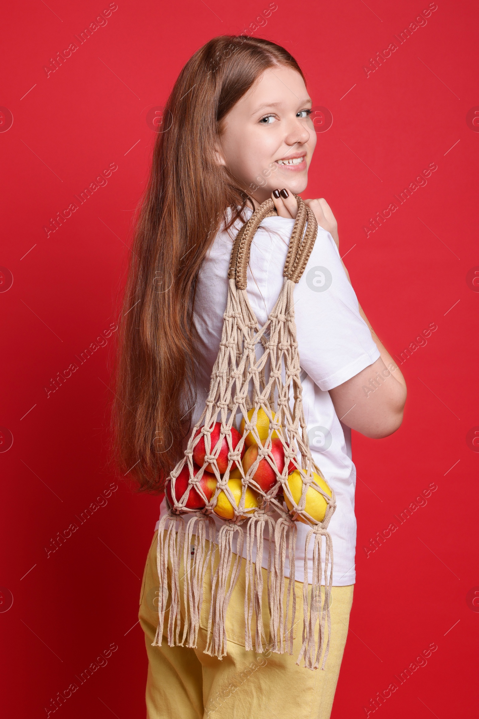 Photo of Teenage girl with handmade macrame bag on red background