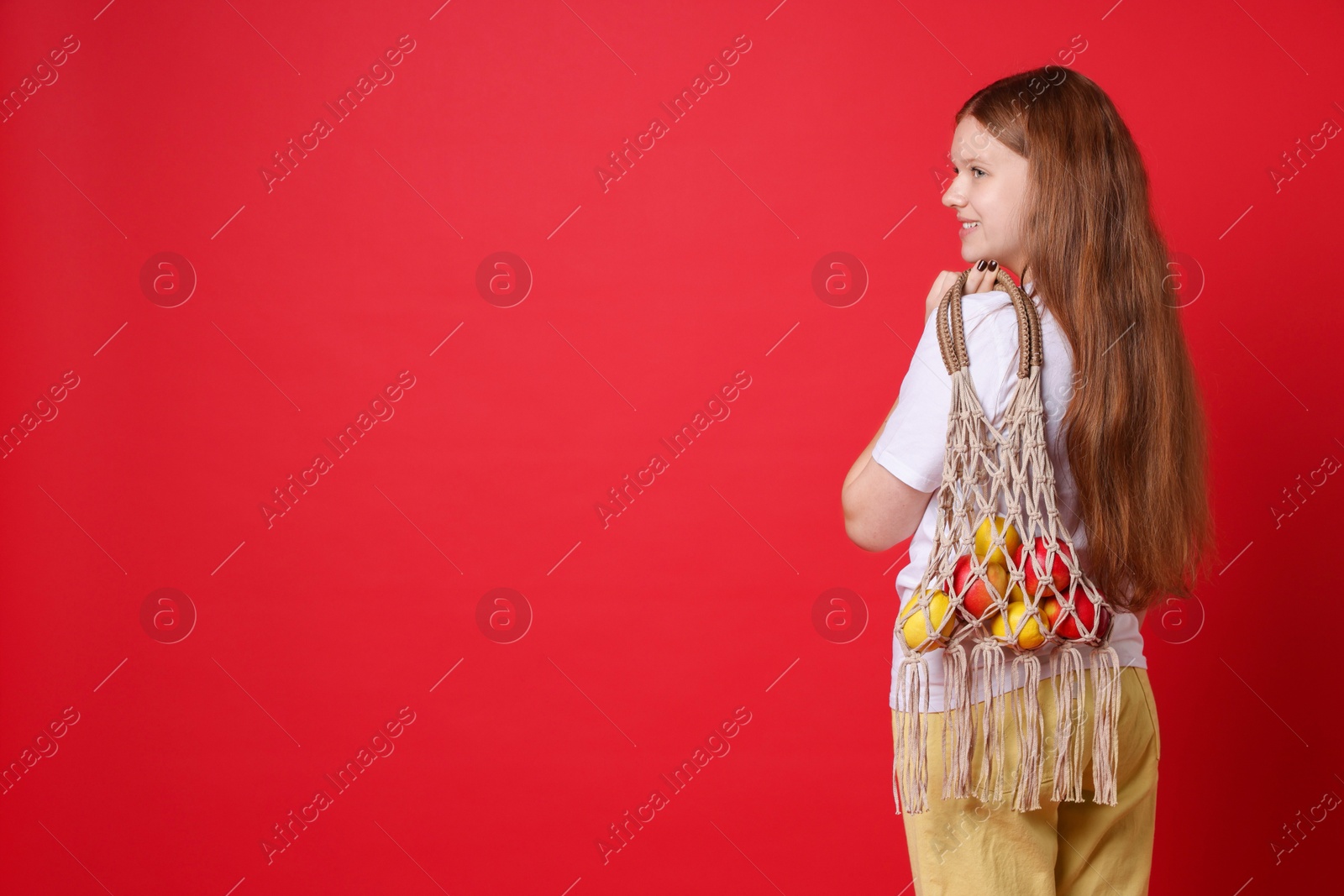 Photo of Teenage girl with handmade macrame bag on red background. Space for text