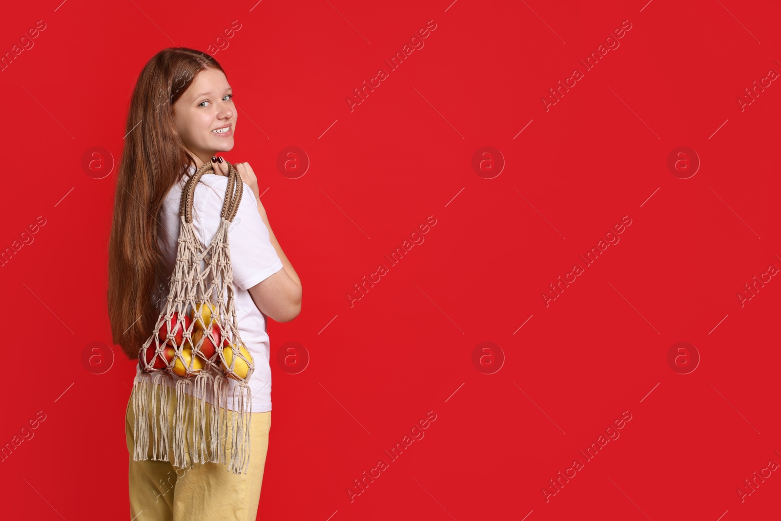 Photo of Teenage girl with handmade macrame bag on red background. Space for text