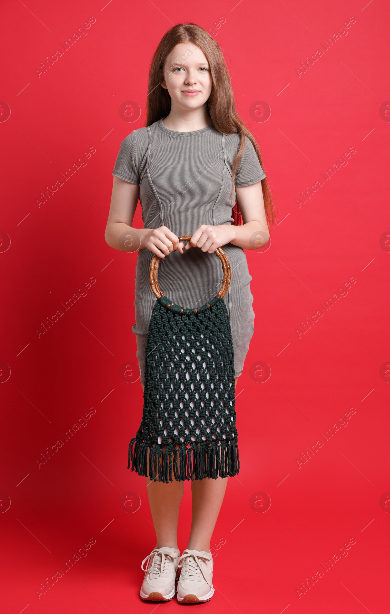 Photo of Teenage girl with handmade macrame bag on red background